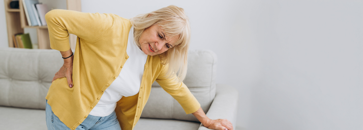 Frau hält sich schmerzenden Rücken: Therapie-Wissen rund um Bandscheibenvorfall