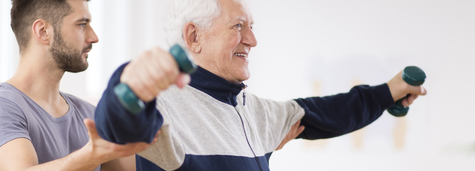 Senior trainiert mit Hanteln unter Anleitung eines Trainers in der Reha