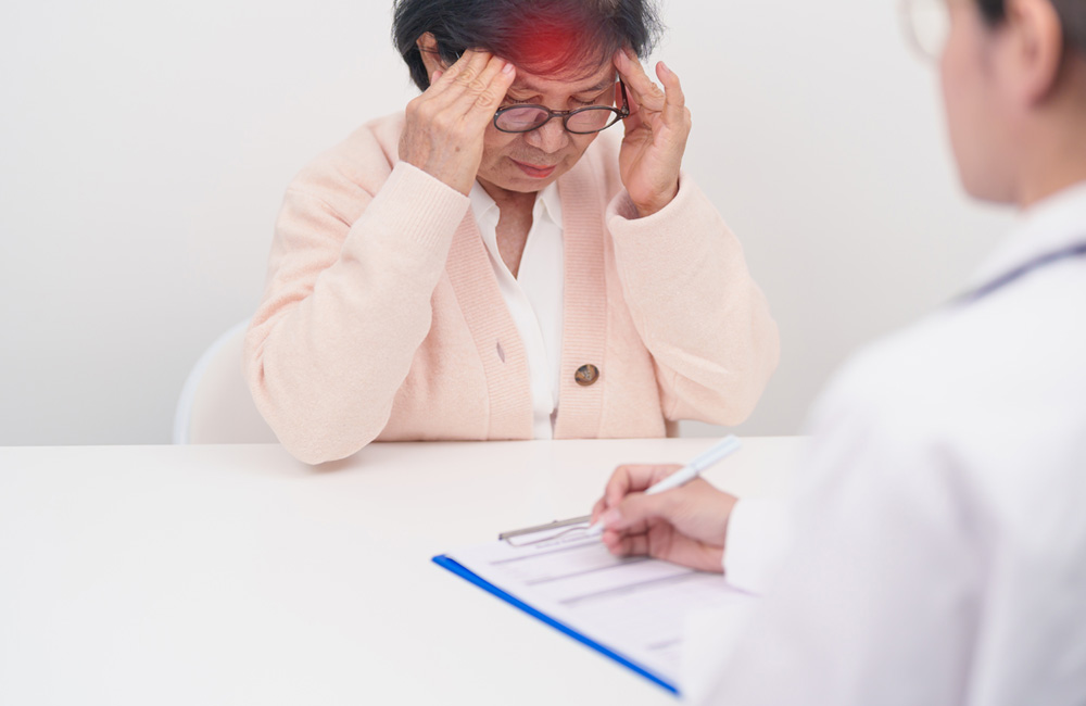 Ältere Frau mit Kopfschmerzen beim Arztgespräch während der Diagnostik