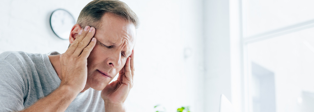 Mann hält sich mit schmerzverzerrtem Gesicht die Schläfen bei Kopfschmerzen