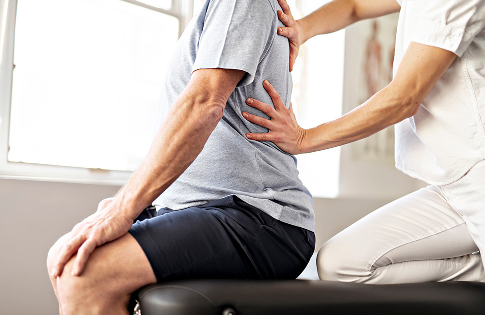 Physiotherapeut untersucht die Wirbelsäule eines sitzenden Patienten