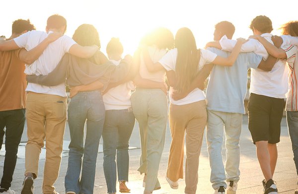 Gruppe junger Menschen geht arm in arm dem Sonnenlicht entgegen