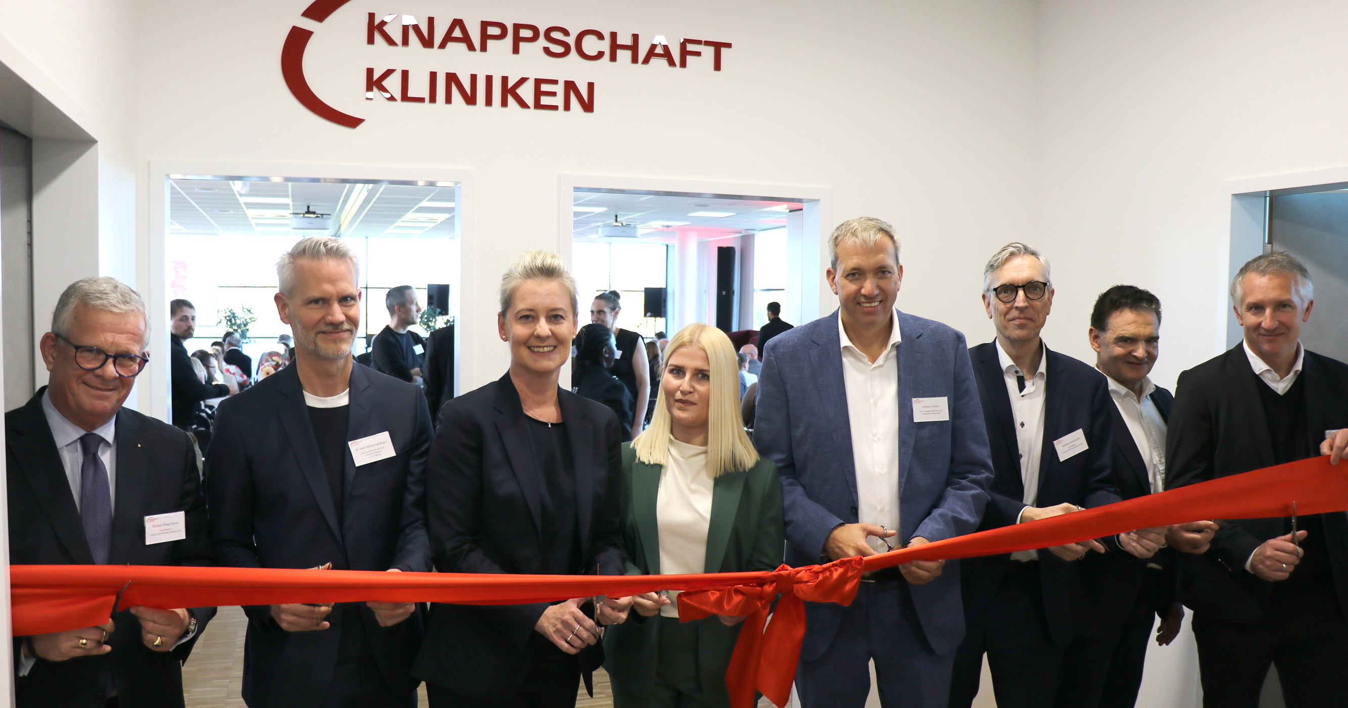 Personen schneiden ein rotes Band vor dem Logo der Knappschaft Kliniken.