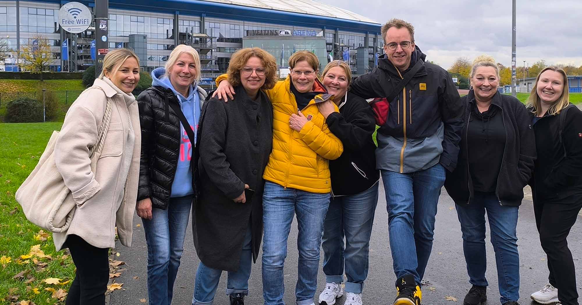 Eine Gruppe von fünf Personen steht lächelnd vor der VELTINS-Arena.