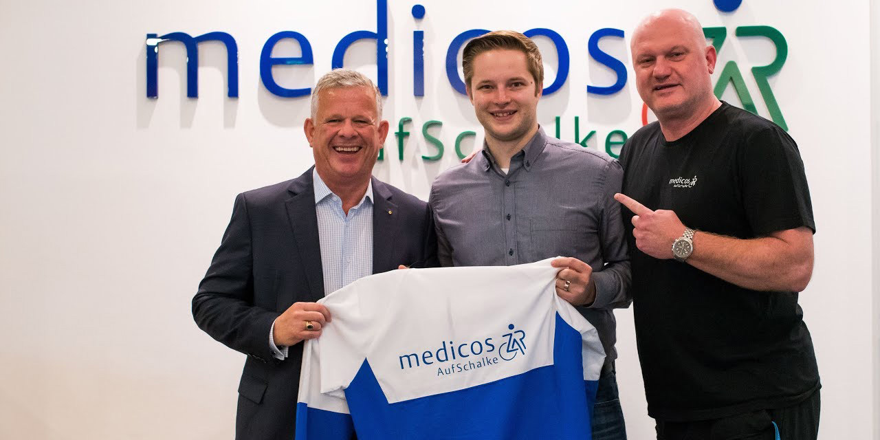 Drei Personen posieren in einer medizinischen Einrichtung mit einem Schalke 04-Basketball-Trikot; die Einrichtung ist als Medicos AufSchalke markiert.