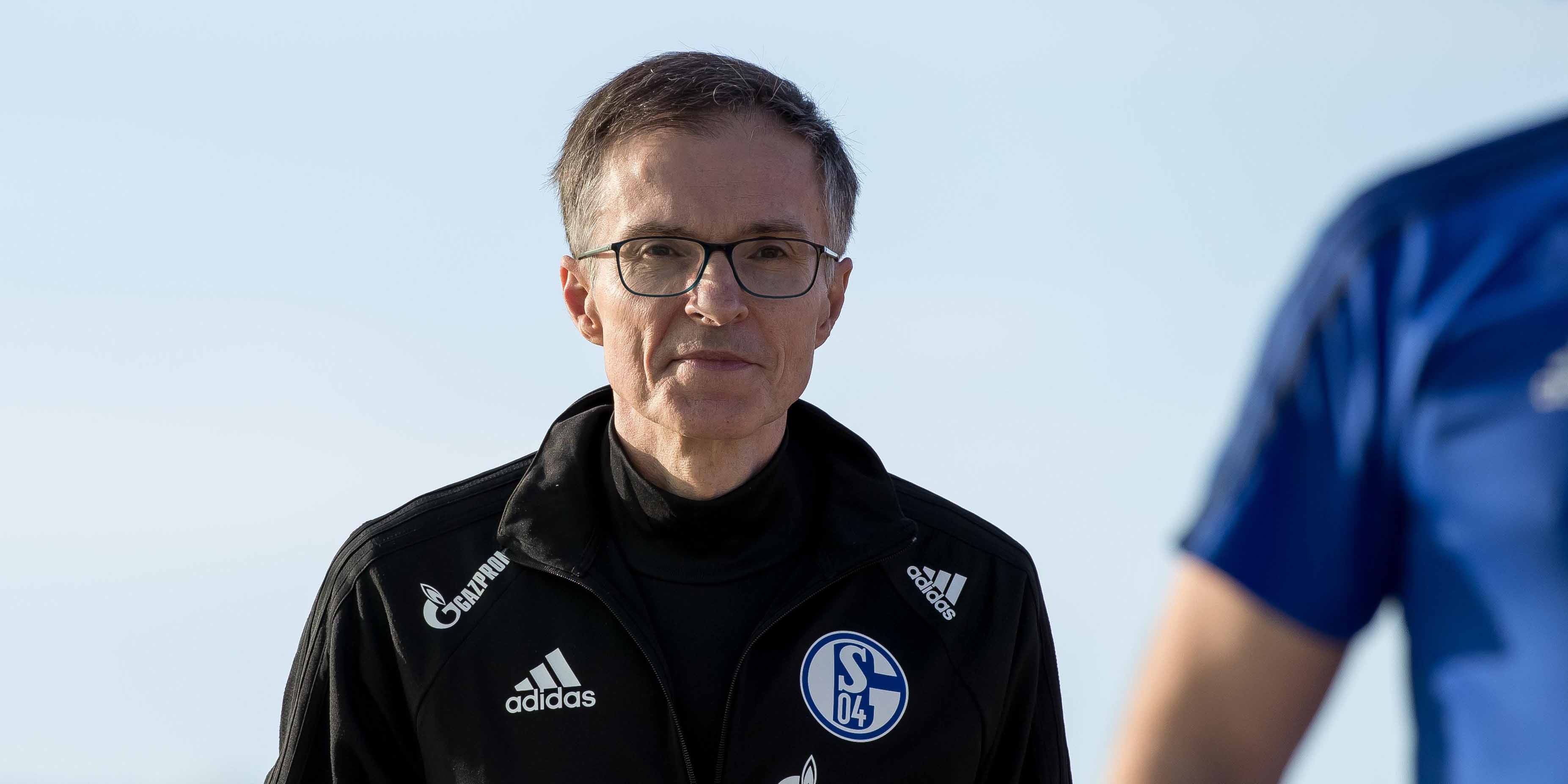 Porträt eines Mannes in einer Schalke 04-Trainingsjacke mit neutralem Hintergrund.